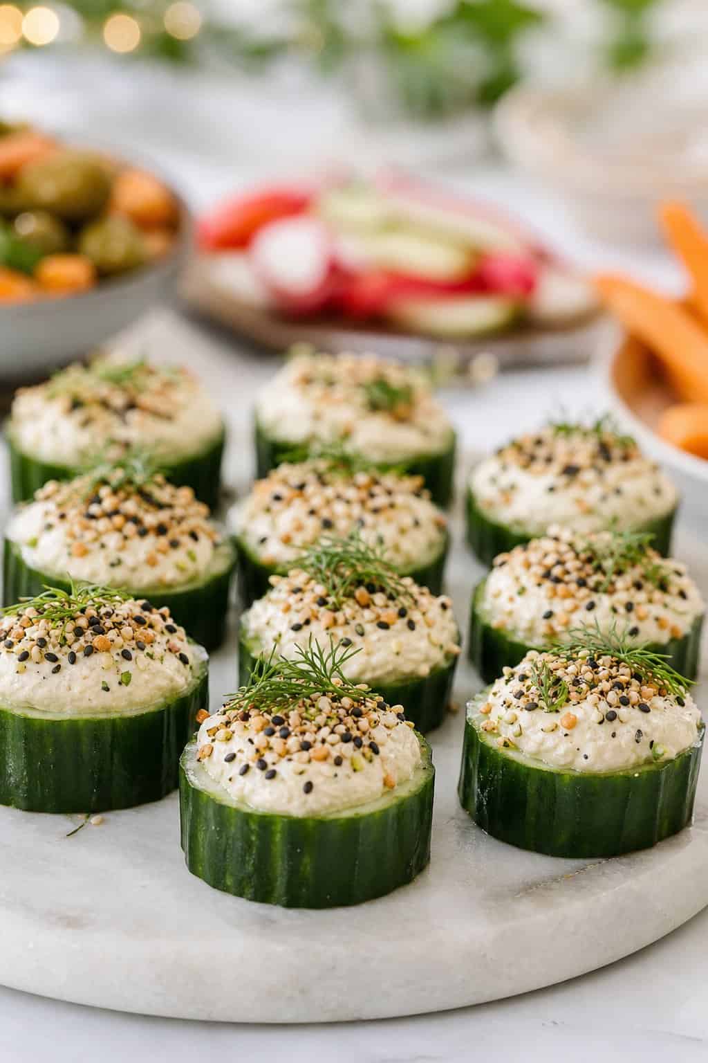 Cucumber slices topped with creamy spread and everything bagel seasoning arranged on a party platter.