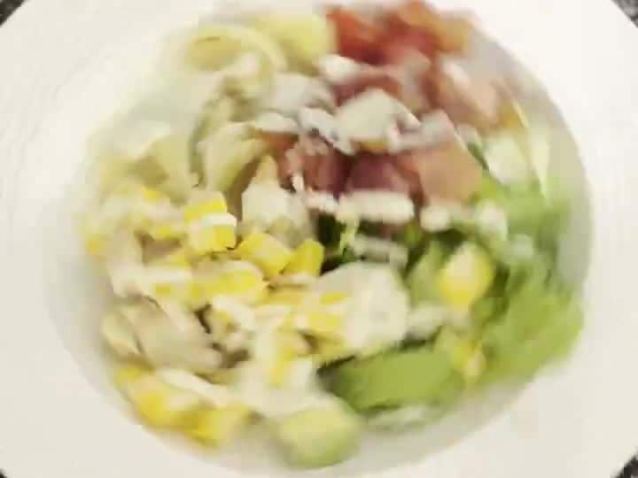 The finished bowl with tortellini, avocado, bacon, corn, and tomato topped with a creamy dressing drizzle.