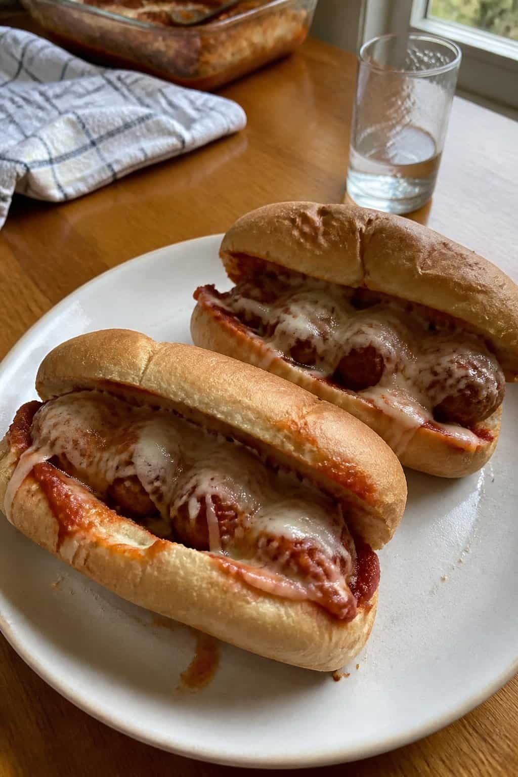 Meatball marinara subs with melted cheese on a plate beside a kitchen window.
