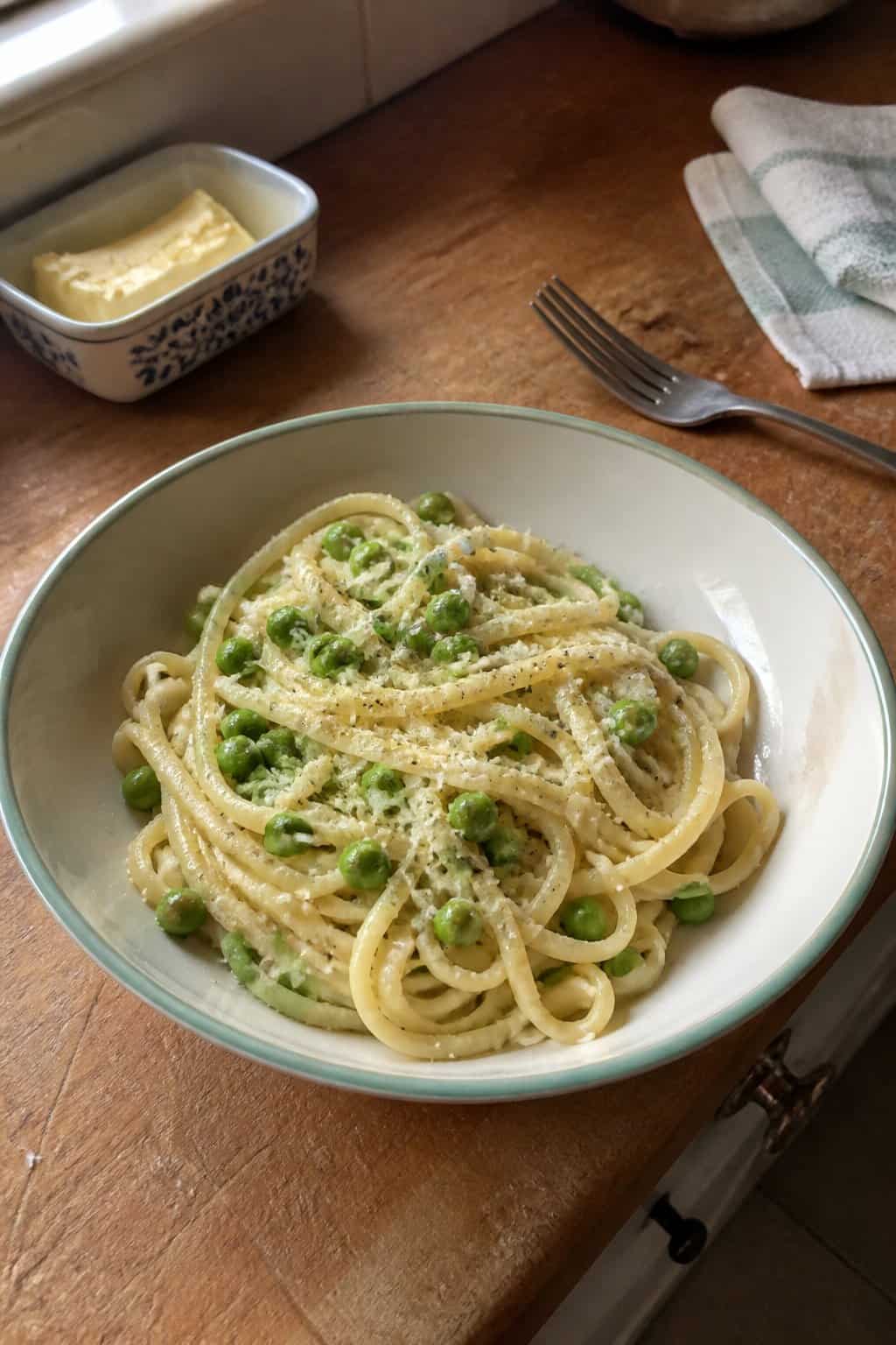 17 Budget Dinners That Use What You Already Bought 13 A bowl of garlic butter pasta with bright green peas on a kitchen table.