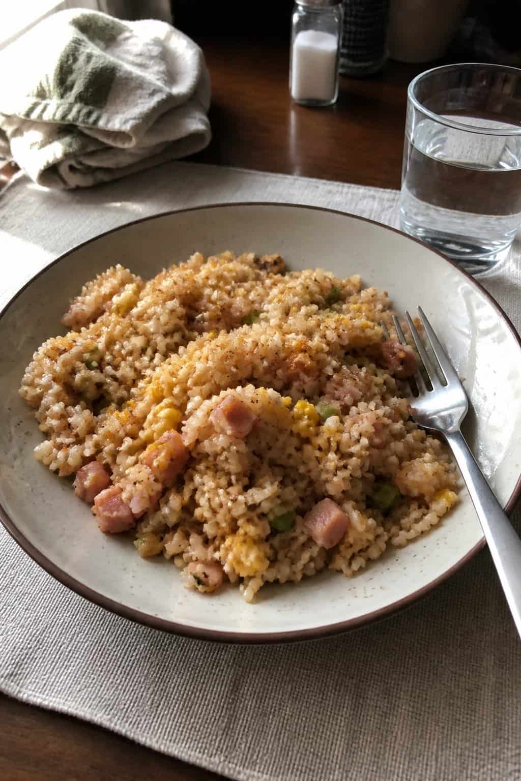 17 Budget Dinners That Use What You Already Bought 11 A bowl of ham and cheese fried rice with scrambled egg and green onion on a kitchen table.