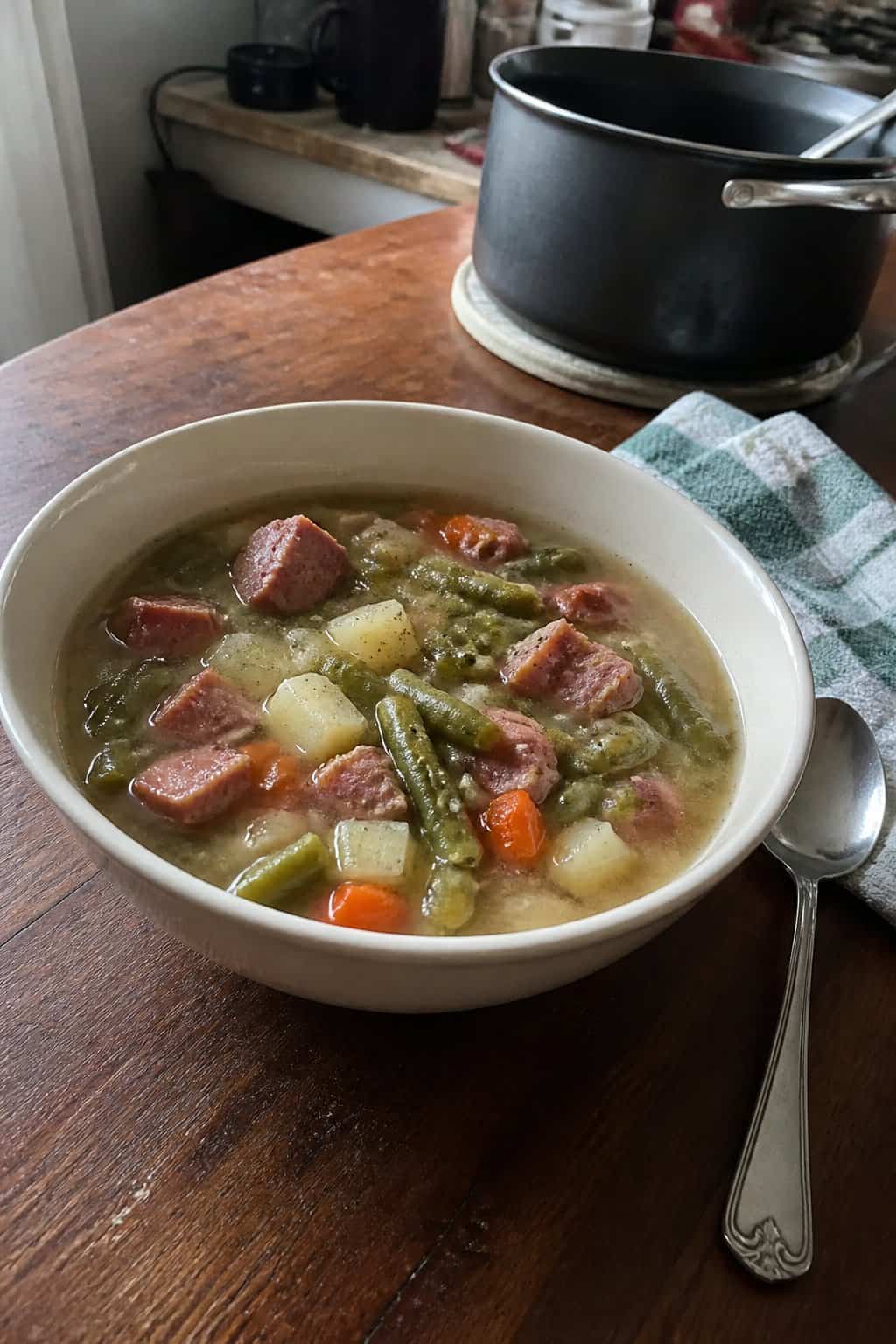 Ham Soup Recipes for Chilly Nights 16 A bowl of ham and green bean soup sits on a kitchen table beside a spoon.
