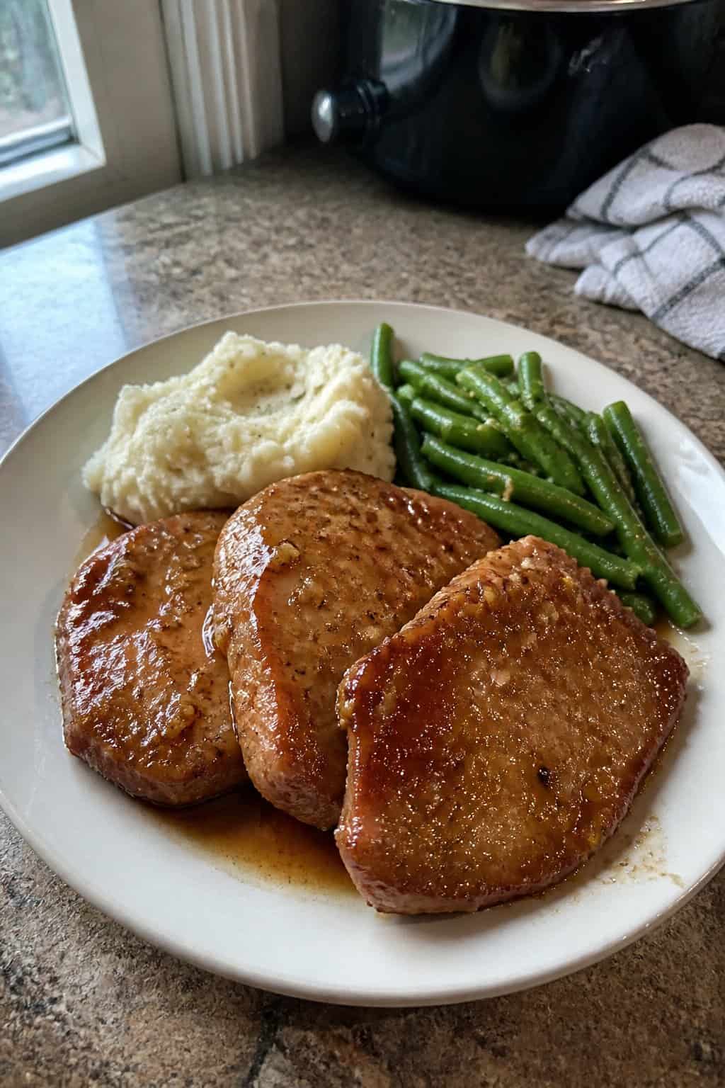 Honey garlic pork chops with mashed potatoes and green beans on a dinner plate.