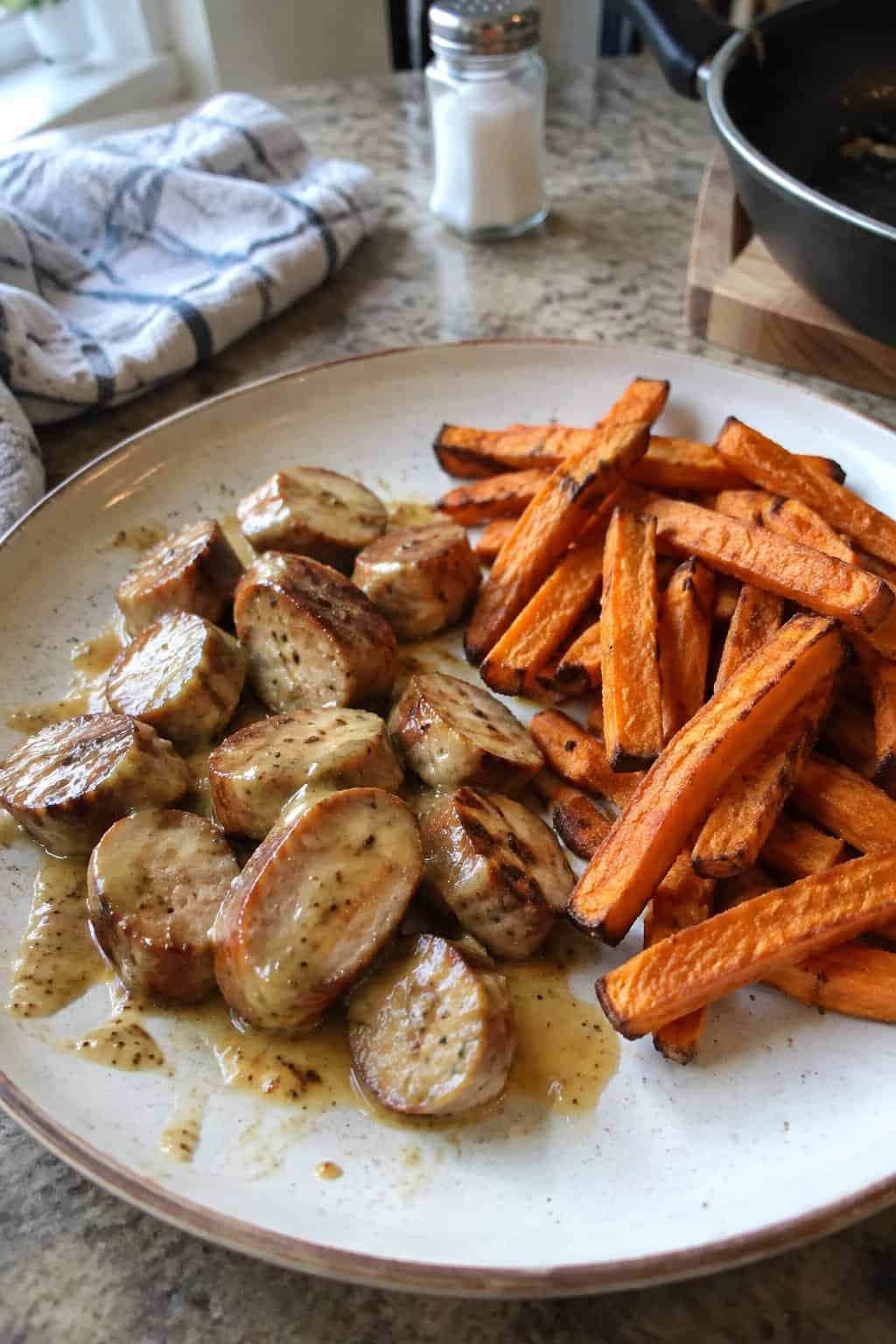 A plate of sliced honey mustard chicken sausage served with sweet potato fries on a kitchen table.