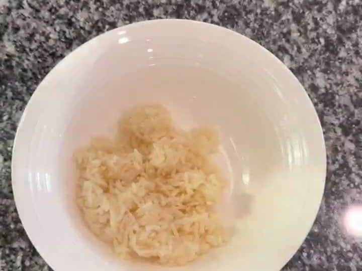 A white bowl containing a portion of jasmine rice as the base layer with chicken pieces on a cutting board nearby.
