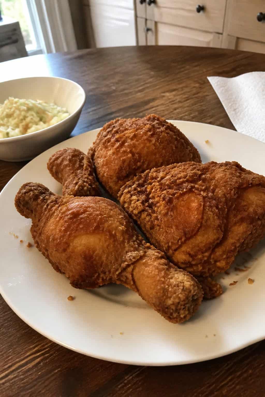 20 Copycat Chicken Recipes for Restaurant Cravings at Home 3 A plate of golden fried chicken sits on a kitchen table beside a simple side dish.
