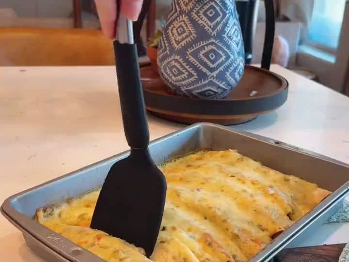 A spatula lifts a golden, cheesy baked enchilada out of the pan showing the finished dish fresh from the oven.