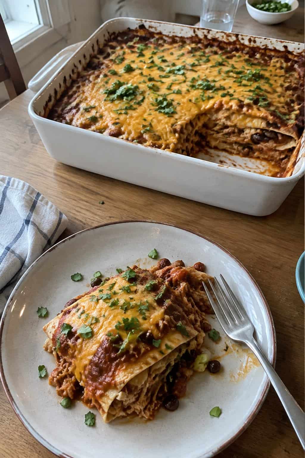 A homemade chicken tortilla casserole with melted cheese is served from a baking dish on a kitchen table.
