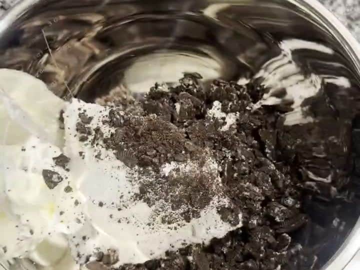 A metal bowl holds crushed Oreo crumbs mixed into a creamy white mixture.