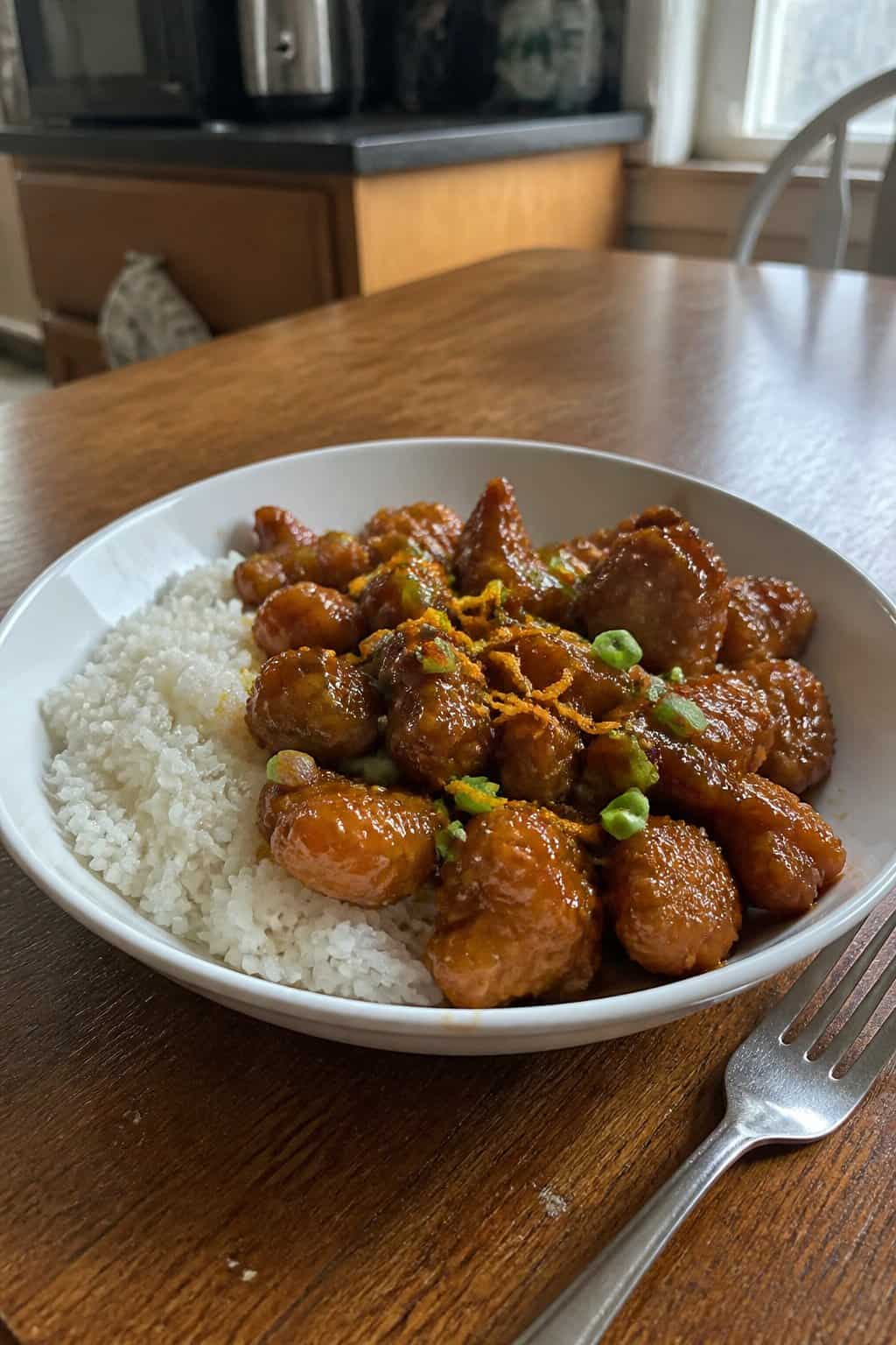20 Copycat Chicken Recipes for Restaurant Cravings at Home 4 A bowl of orange-glazed chicken with white rice on a kitchen table.