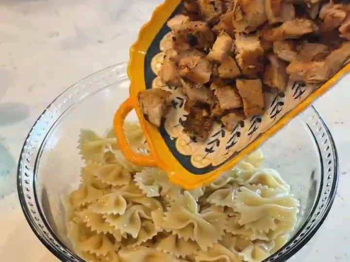 Greek Chicken Pasta Salad 5 Cooked bow tie pasta being poured from a cutting board into a glass bowl.