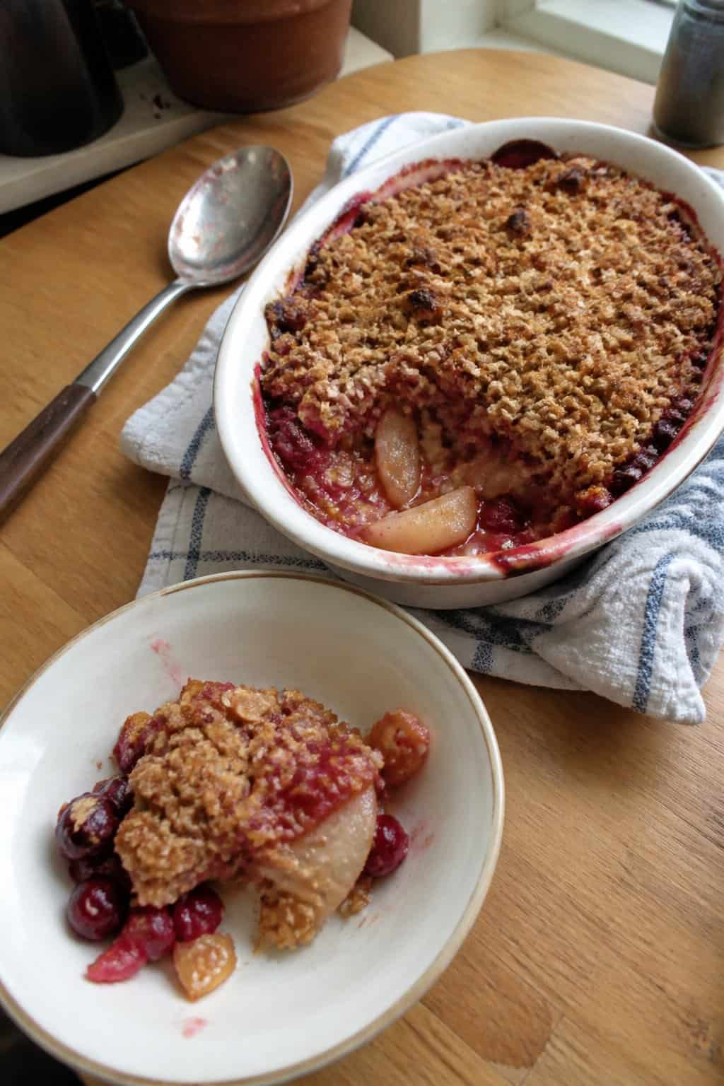 A golden pear and cranberry crumble in a baking dish beside a single serving in a bowl.