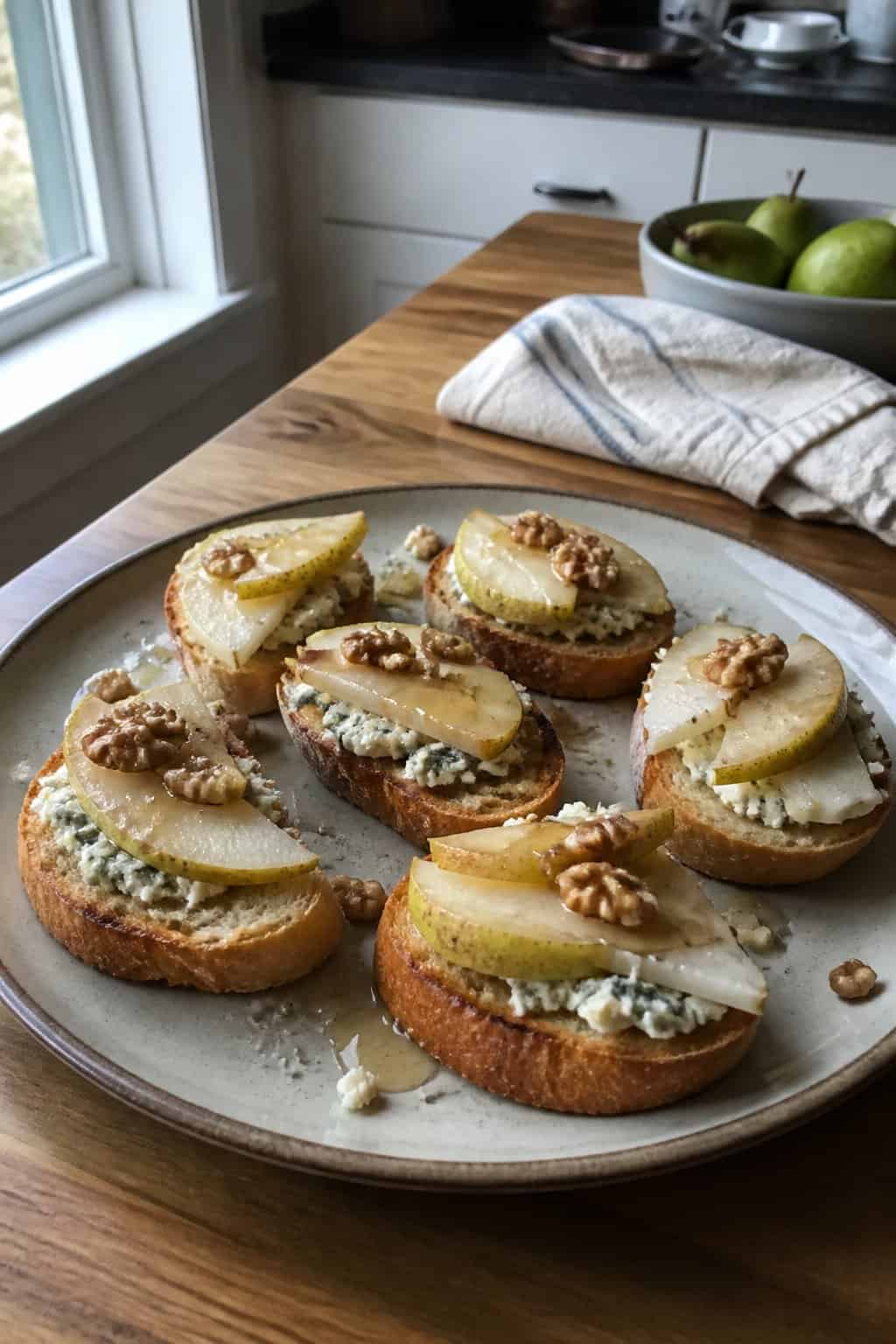 A plate of pear and Gorgonzola crostini with walnuts and honey on a kitchen table.