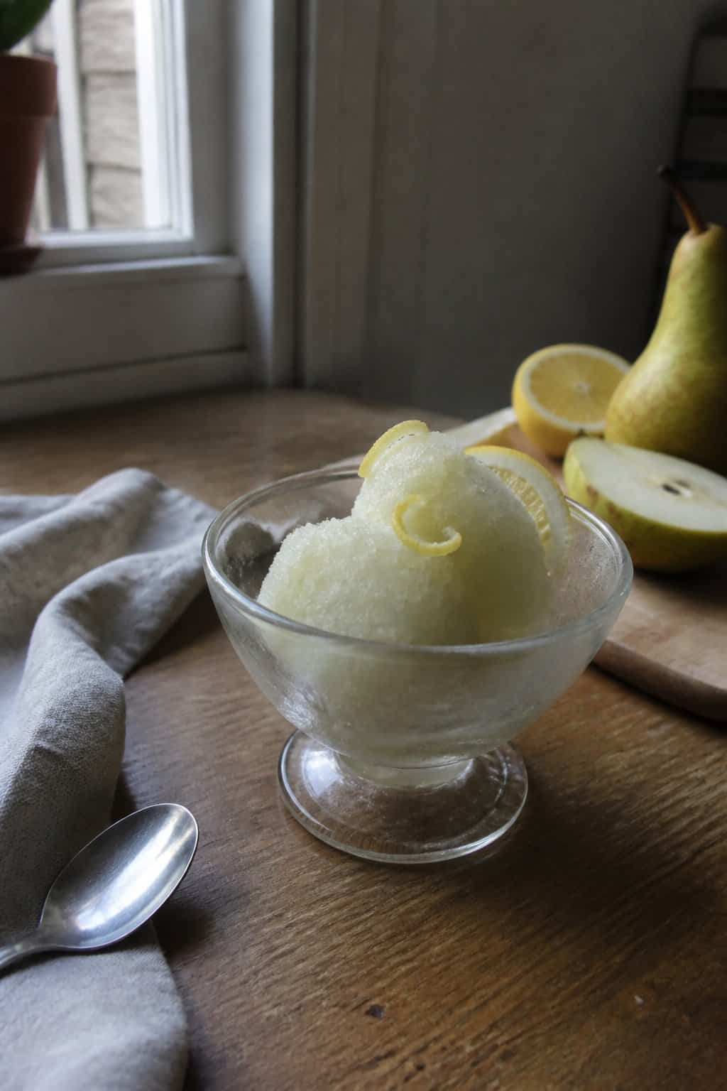 A bowl of pale pear sorbet garnished with lemon on a kitchen table.