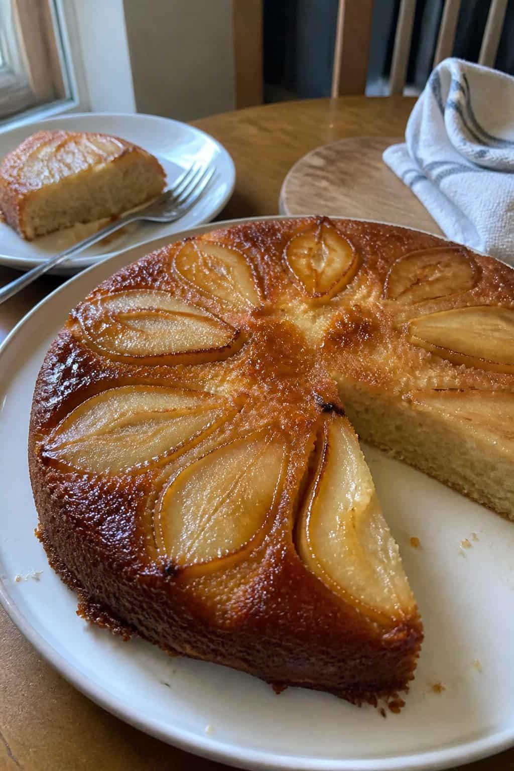 A homemade pear upside-down cake with caramelized pears sits on a plate beside a fork.