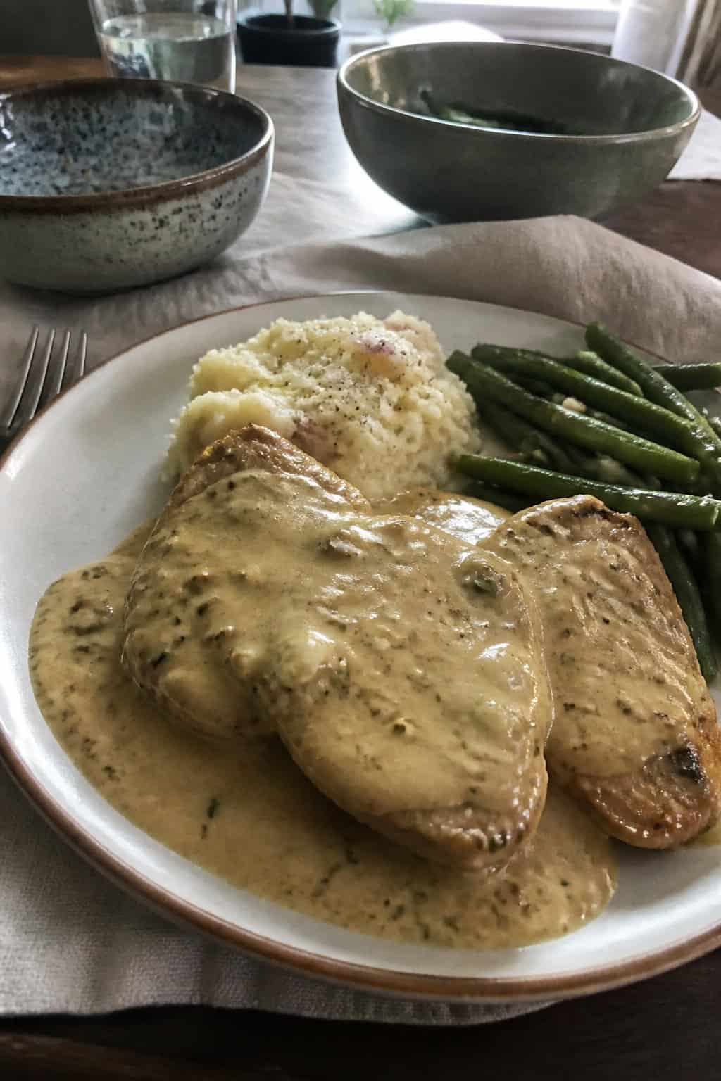 A plate of boneless pork chops covered in creamy Dijon sauce with mashed potatoes and green beans.
