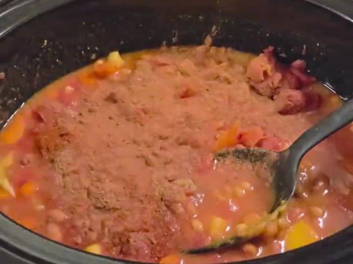 Slow Cooker Pumpkin Lentil Chili with Cinnamon and Nutmeg 6 The thick orange-red chili sits in the slow cooker with a spoon resting in it after mixing in spices.