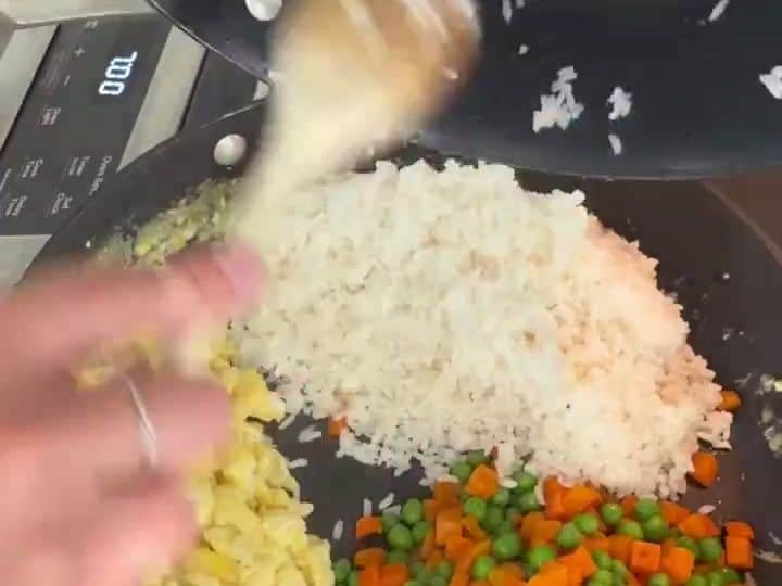 Easy Chicken Fried Rice 5 Rice, peas and carrots, and scrambled egg are being combined together in a skillet with a wooden spoon.