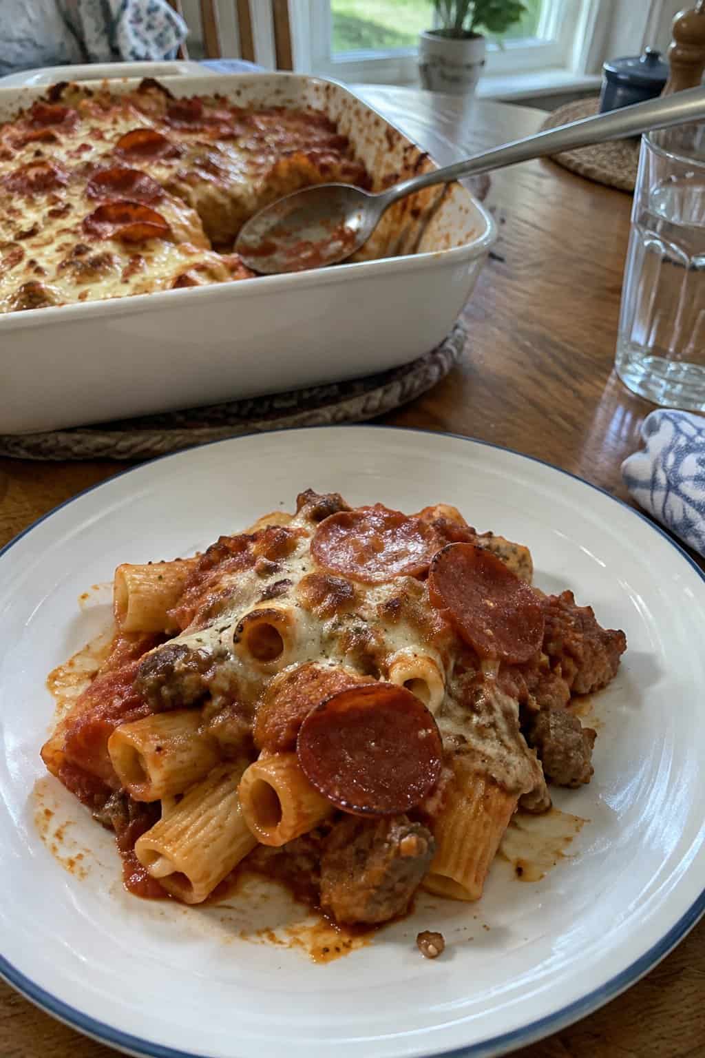 A serving of sausage and pepperoni pasta bake on a plate beside a casserole dish.