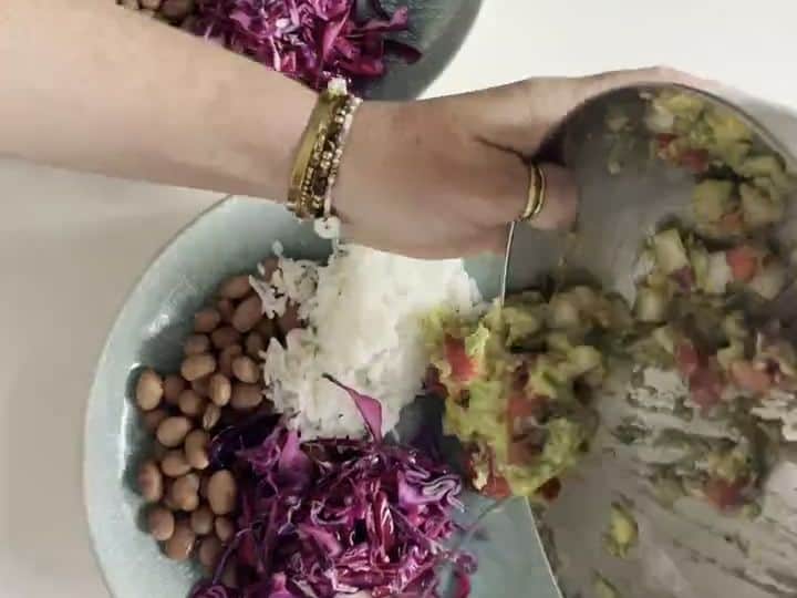 Veggie Burrito Bowls with Taco-Seasoned Guacamole 5 A hand scoops guacamole onto a bowl already containing rice, beans, and shredded cabbage.