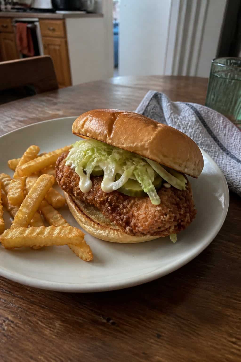 20 Copycat Chicken Recipes for Restaurant Cravings at Home 20 A homemade crispy chicken sandwich with lettuce and fries on a plate beside a kitchen table.