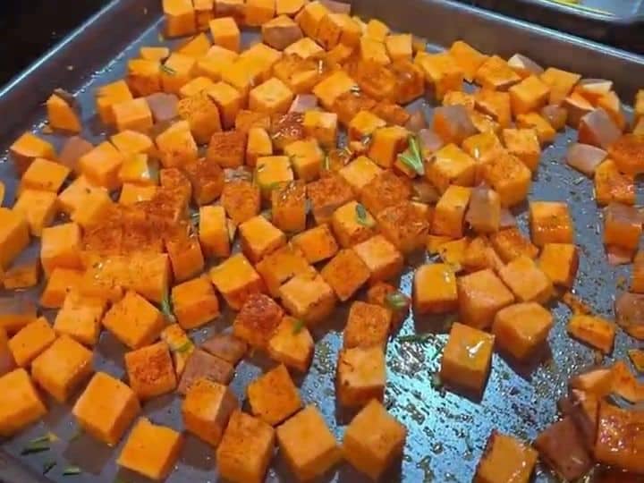 30-Minute Sheet Pan Flounder with Sweet Potatoes and Rainbow Carrots 4 A sheet pan holds roasted diced sweet potatoes while a hand adds brussels sprouts and carrot pieces beside them.