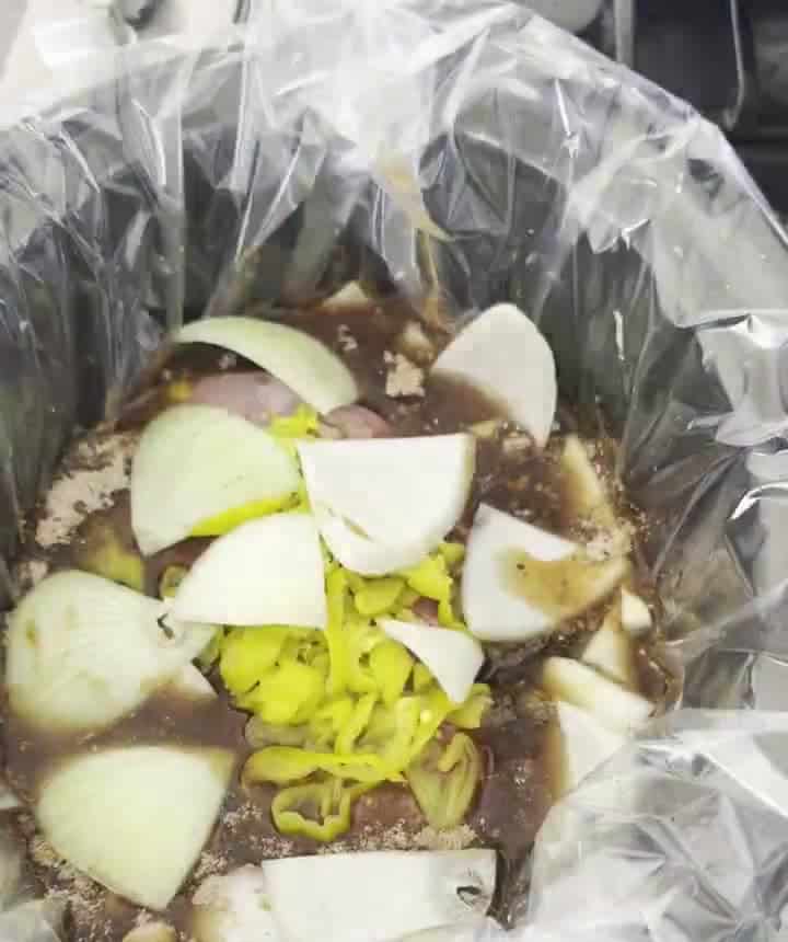 Chuck roast in broth and enchilada sauce topped with pepperoncini peppers and onion wedges in a slow cooker