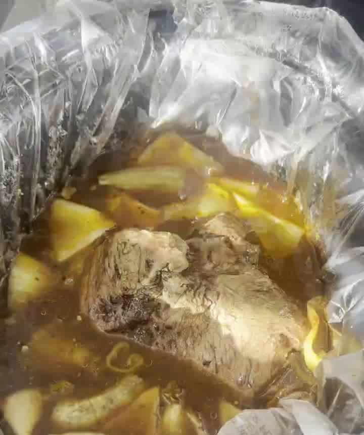 Cooked fork-tender chuck roast sitting in dark birria broth with onions and pepperoncini in the slow cooker