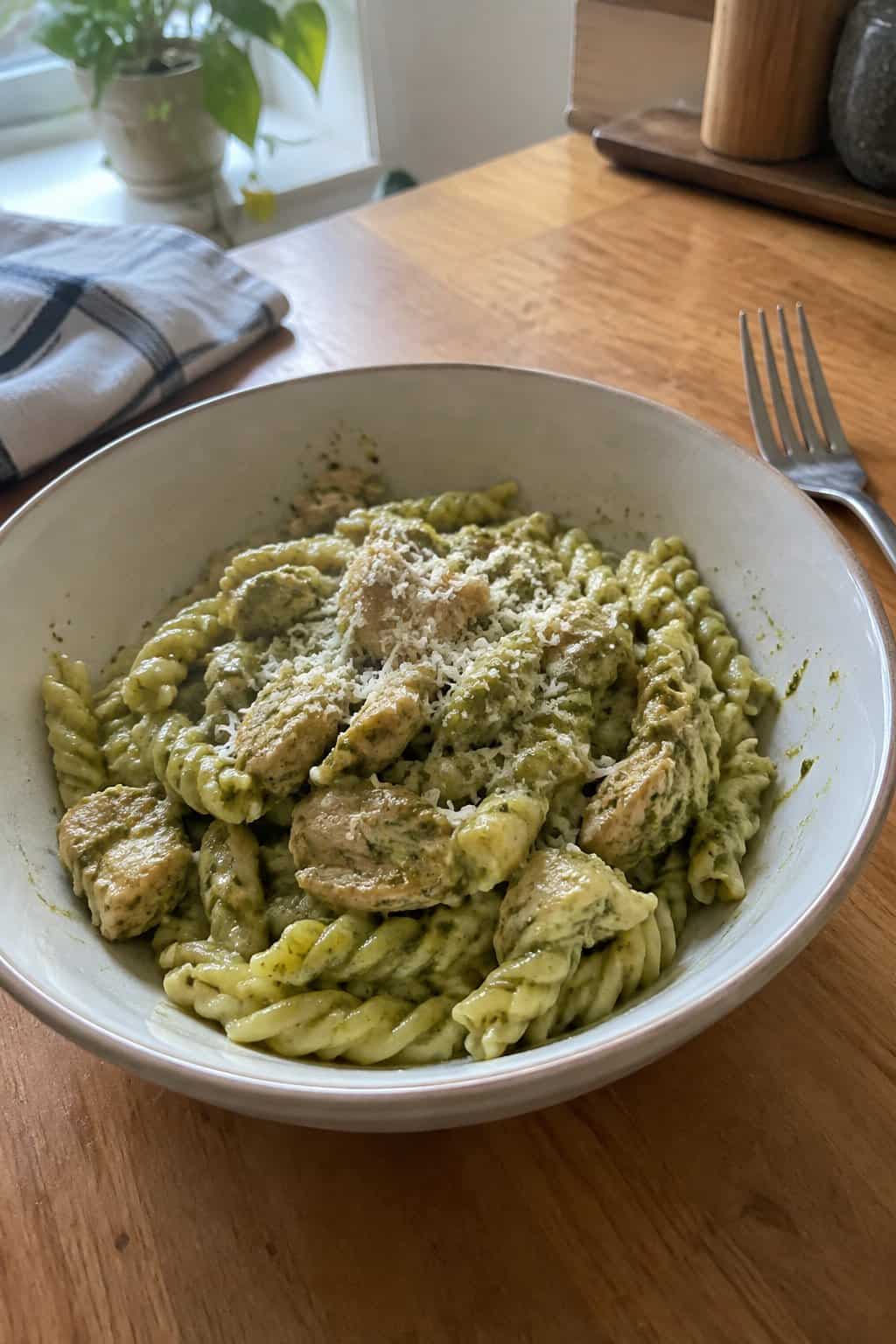 Twisted gemelli pasta coated in a green pesto cream sauce with pieces of chicken throughout.