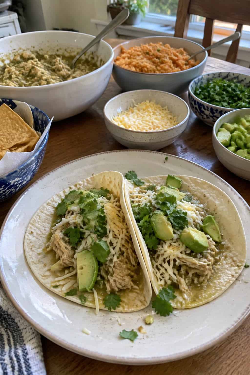 Soft tacos filled with shredded salsa verde chicken and simple toppings on a plate.