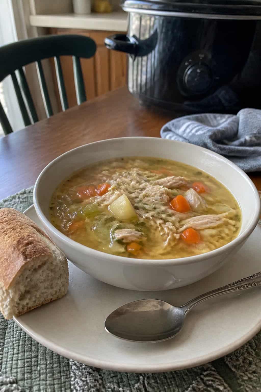 25 Turkey Soup Recipes That Make the Whole House Smell Amazing 5 A bowl of turkey vegetable soup with carrots, celery, potatoes, and herbs on a kitchen table.