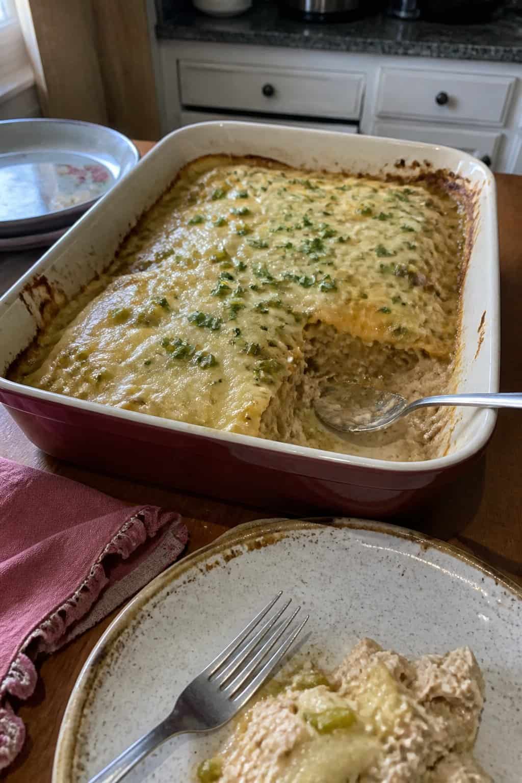 A serving of creamy chicken enchilada casserole in a ceramic baking dish on a kitchen table.