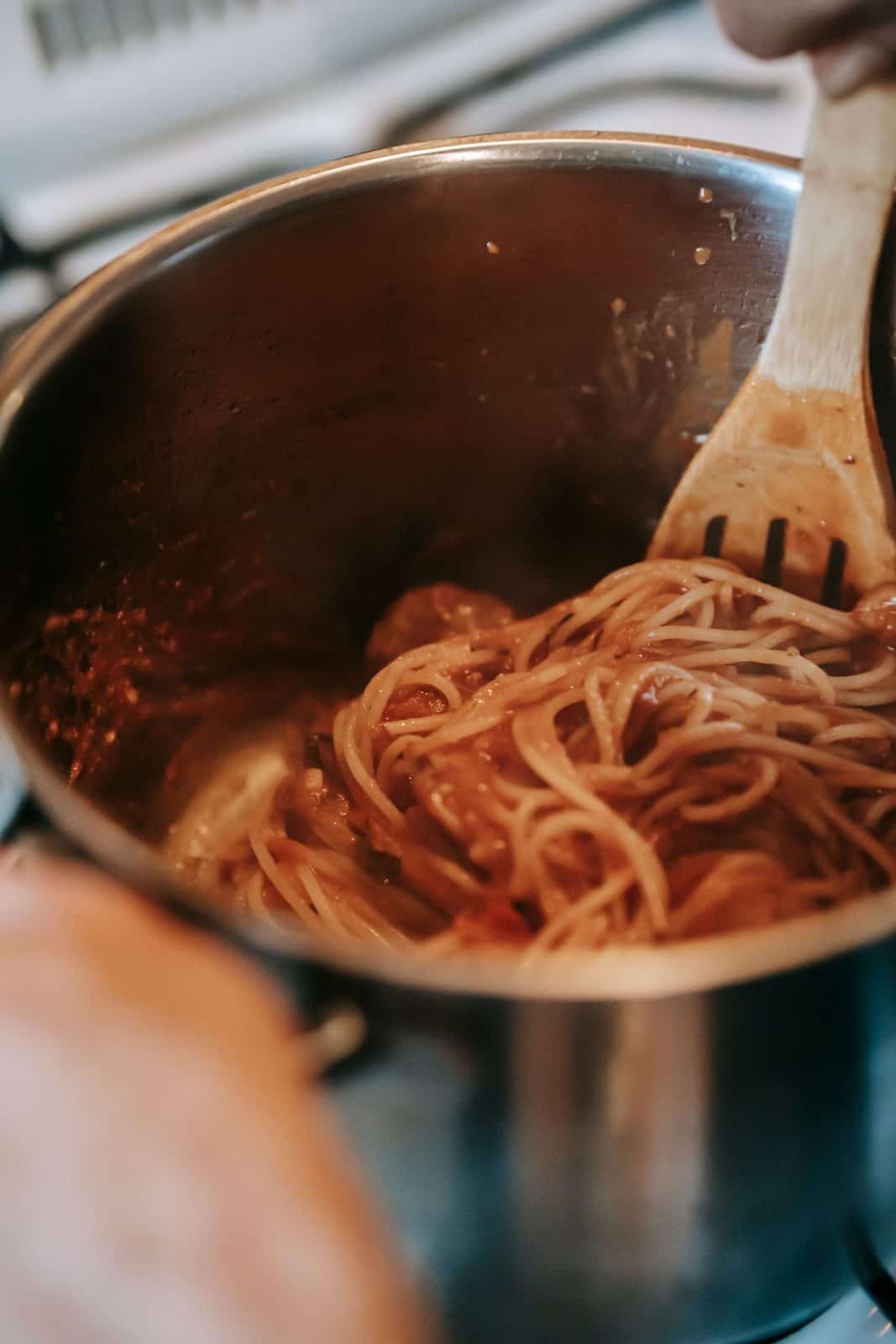 Spaghetti in tomato sauce being stirred with a wooden spoon in a metal saucepan