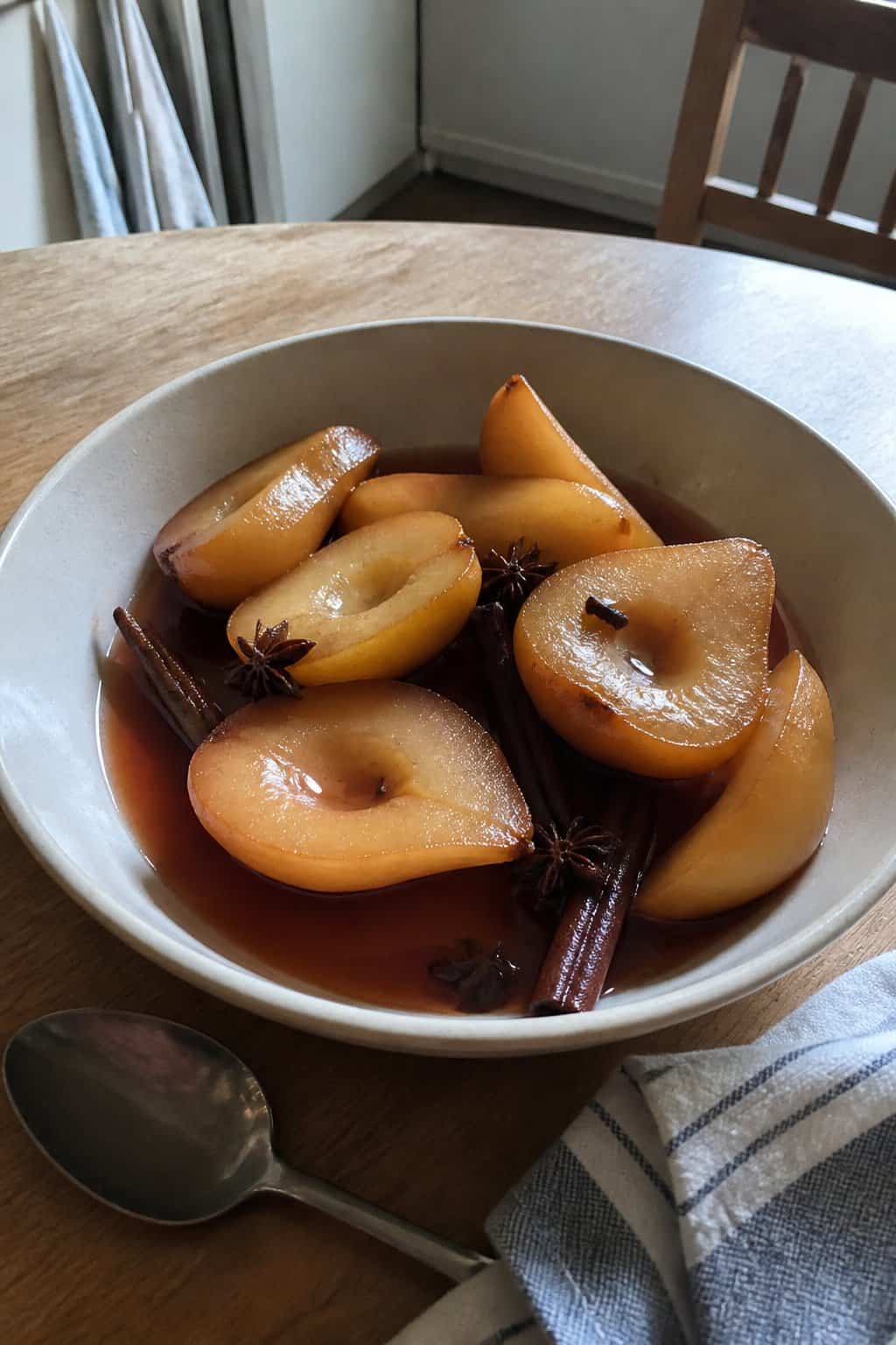 A bowl of homemade poached pear pieces in spiced syrup with cinnamon sticks and star anise.