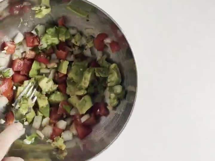 Veggie Burrito Bowls with Taco-Seasoned Guacamole 4 A hand stirs a metal bowl of diced avocado, tomato, onion, and cilantro seasoned with taco spice.