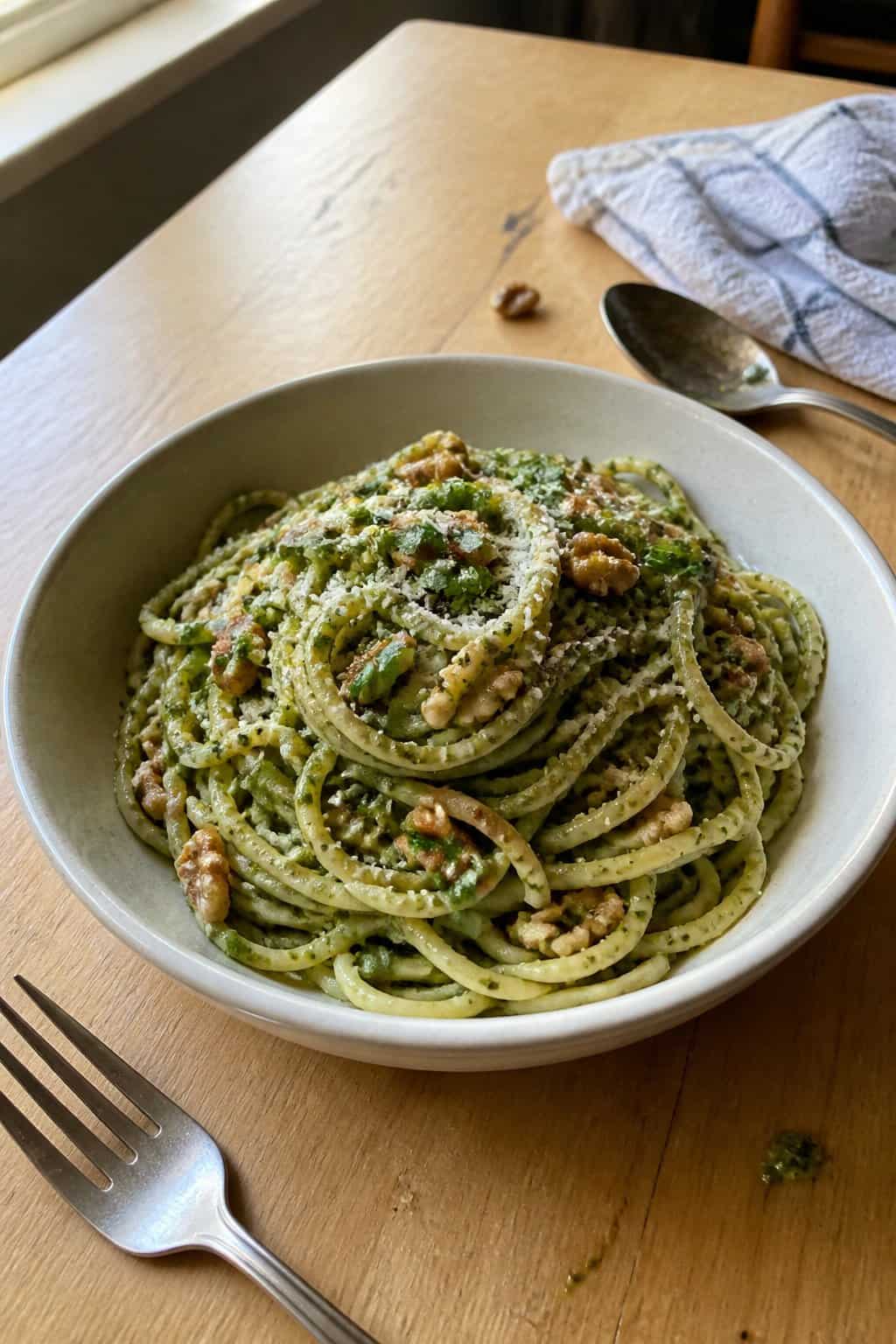 17 Pasta Dinners That Feel Fancy But Use Pantry Staples 15 A bowl of green pesto pasta scattered with toasted walnut pieces, resting beside a fork