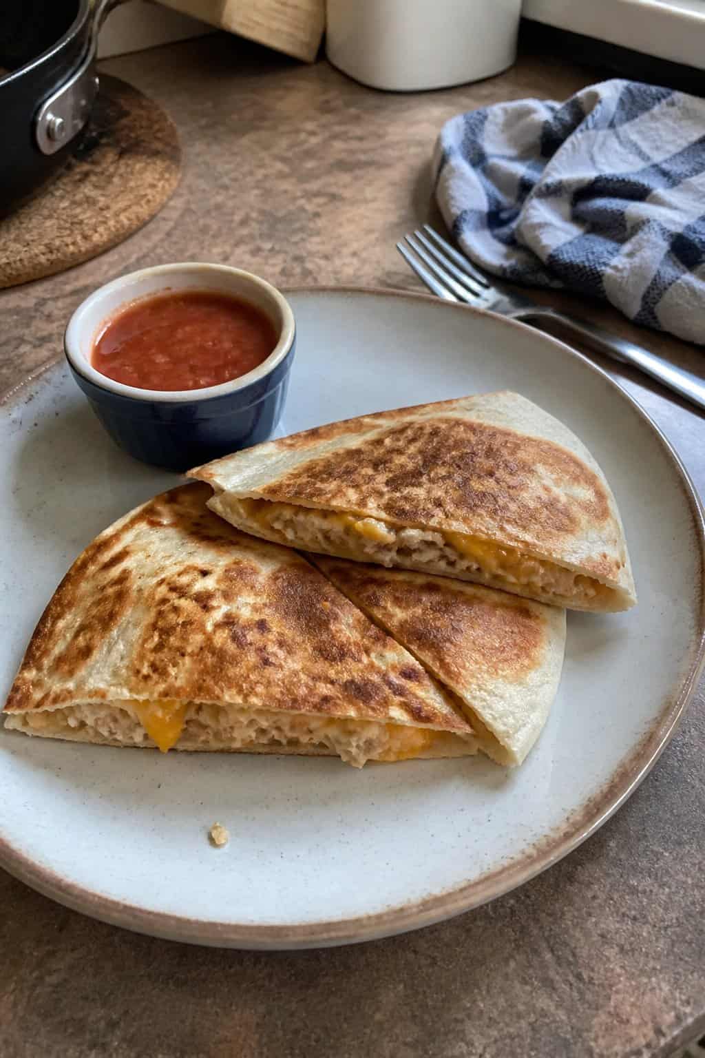 17 Budget Dinners That Use What You Already Bought 5 Golden-brown tuna melt quesadilla wedges on a plate next to a small bowl of dipping sauce.