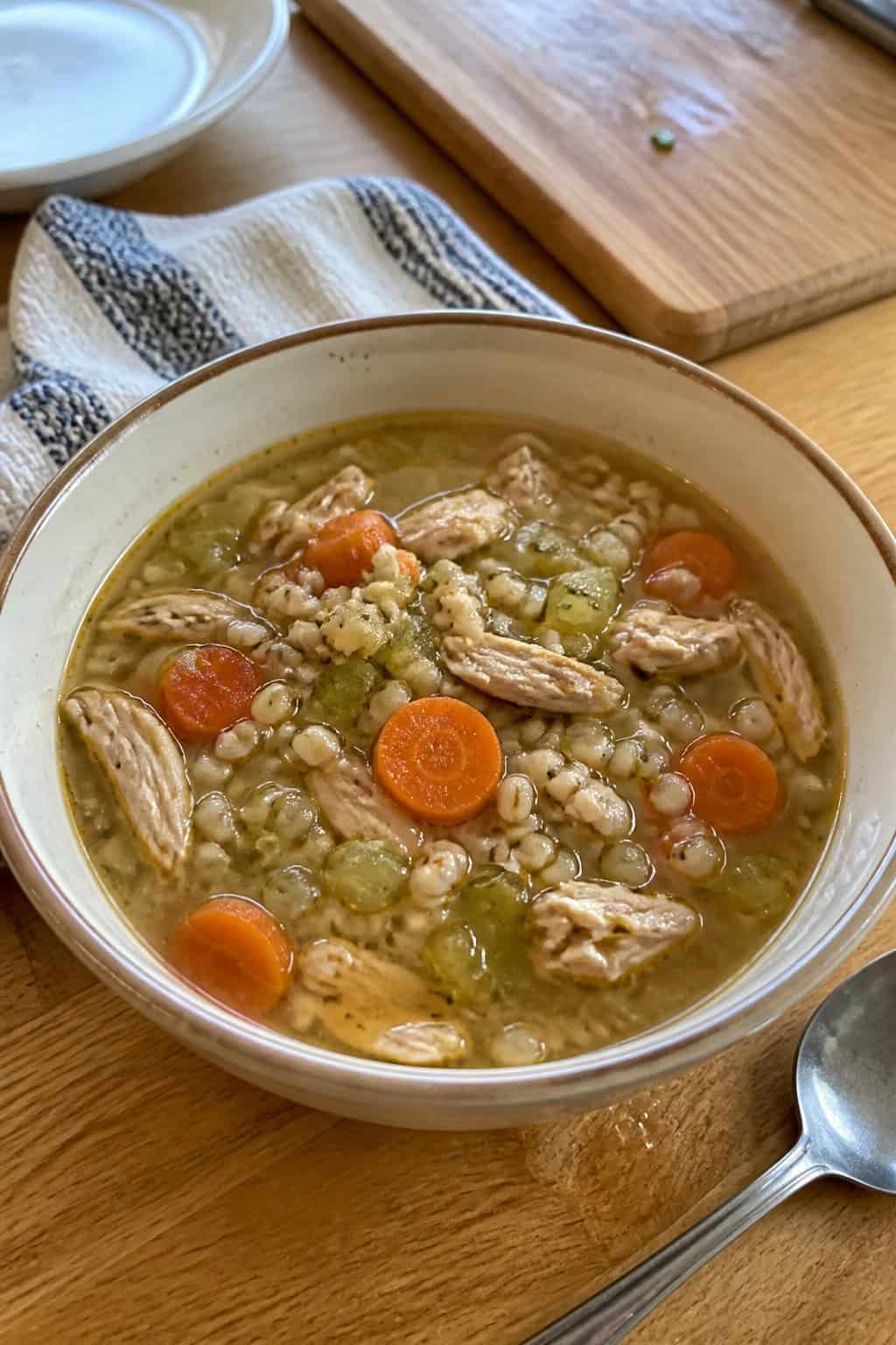 25 Turkey Soup Recipes That Make the Whole House Smell Amazing 11 A bowl of homemade turkey barley soup with carrots and celery on a kitchen table.