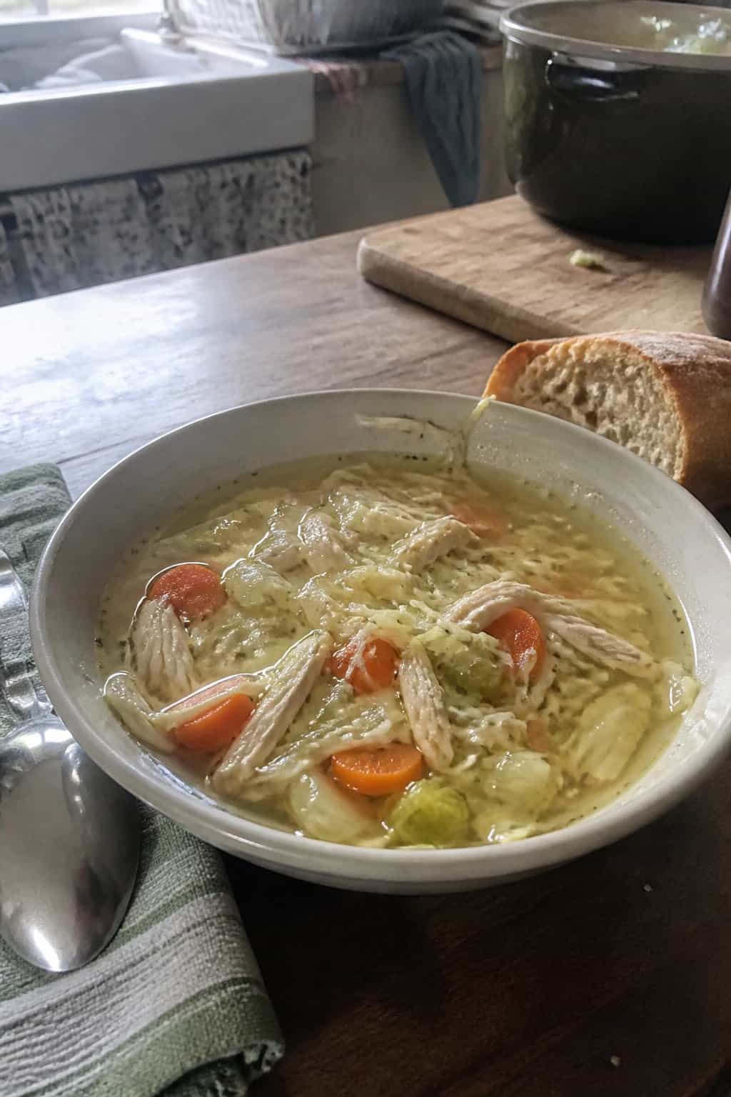 25 Turkey Soup Recipes That Make the Whole House Smell Amazing 27 A bowl of homemade turkey and cabbage soup with vegetables on a kitchen table beside bread and a spoon.