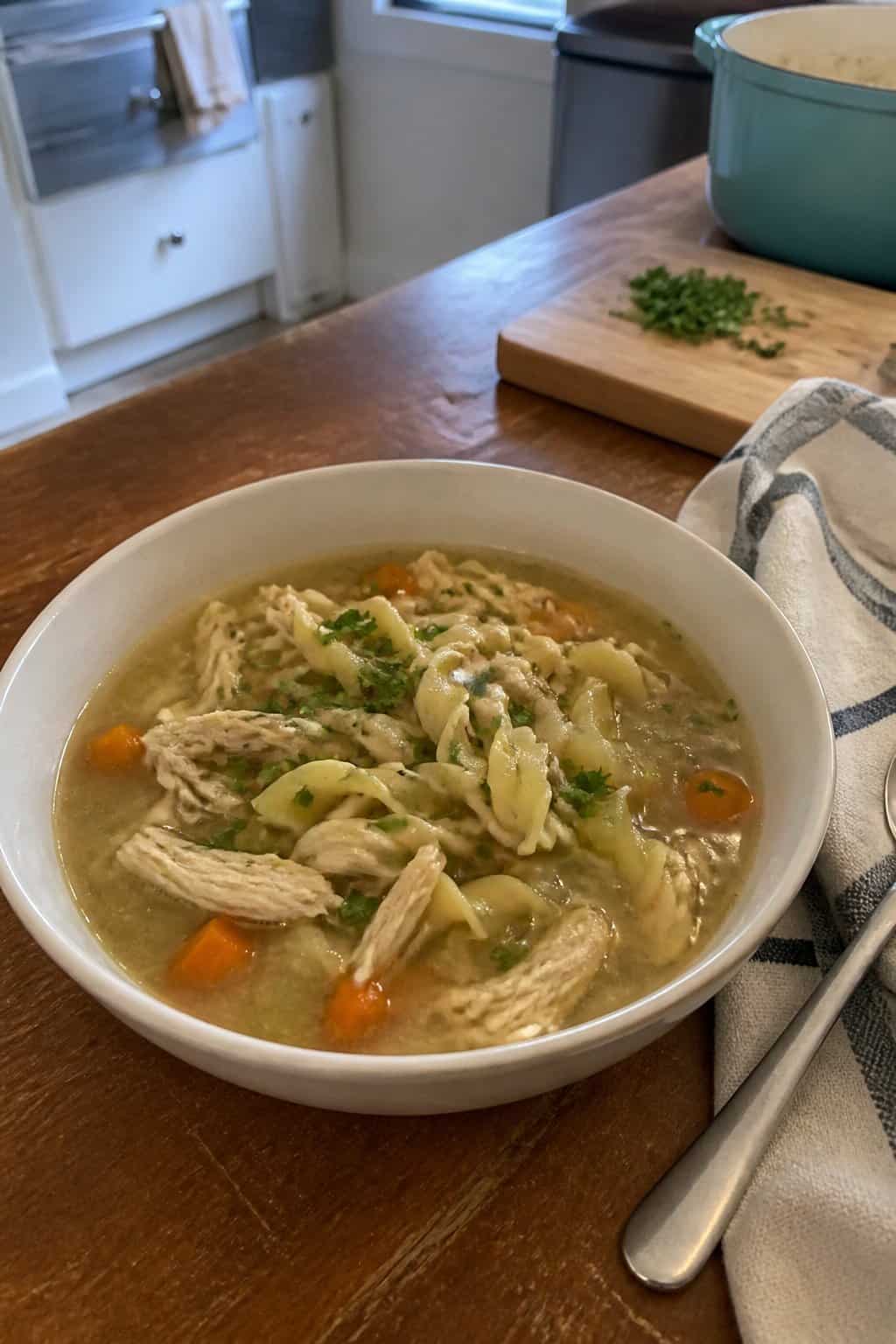 25 Turkey Soup Recipes That Make the Whole House Smell Amazing 4 A bowl of homemade turkey noodle soup with egg noodles, vegetables, and parsley on a kitchen table.