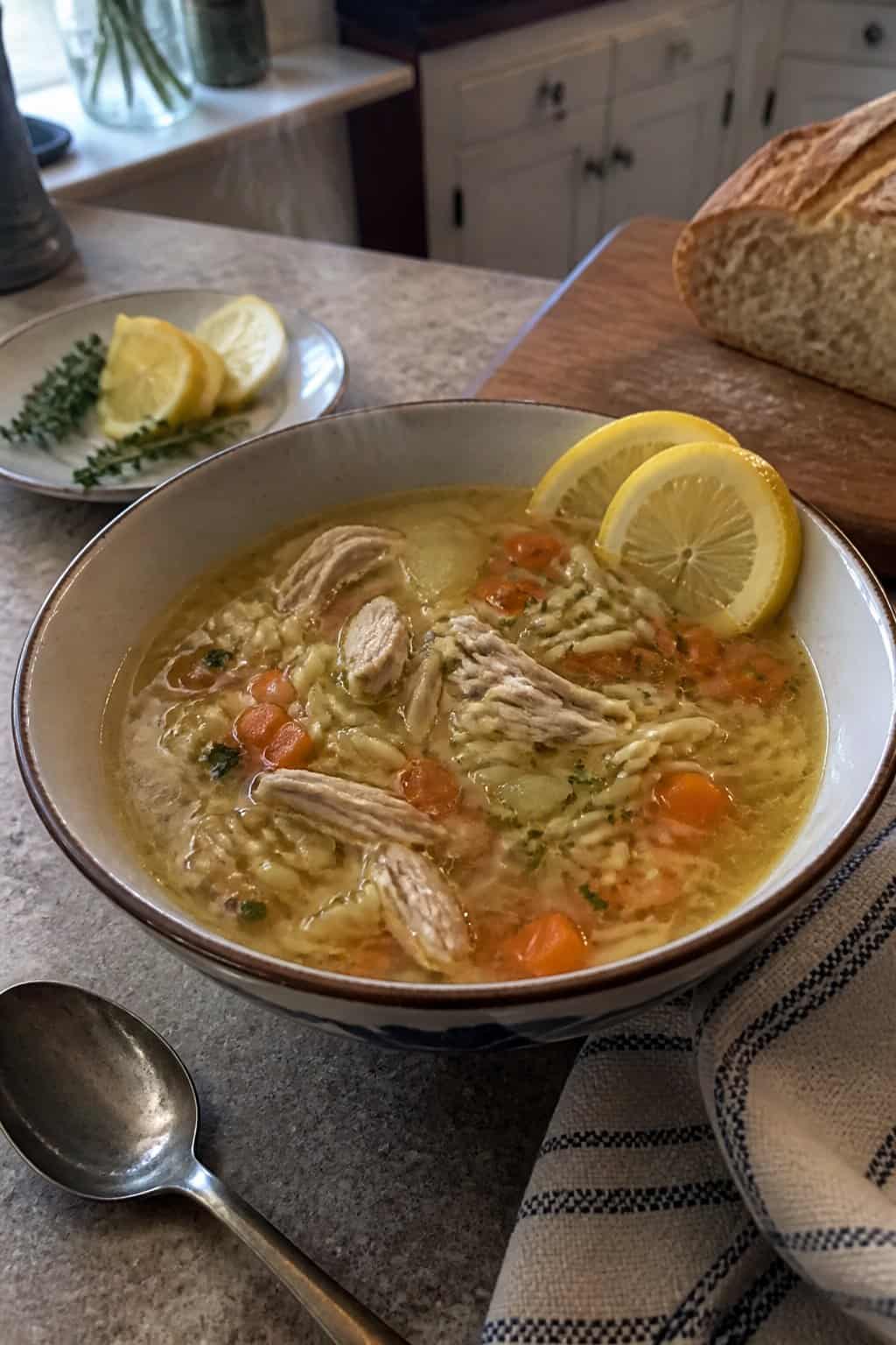 25 Turkey Soup Recipes That Make the Whole House Smell Amazing 14 A bowl of turkey orzo soup with vegetables and lemon on a kitchen table.