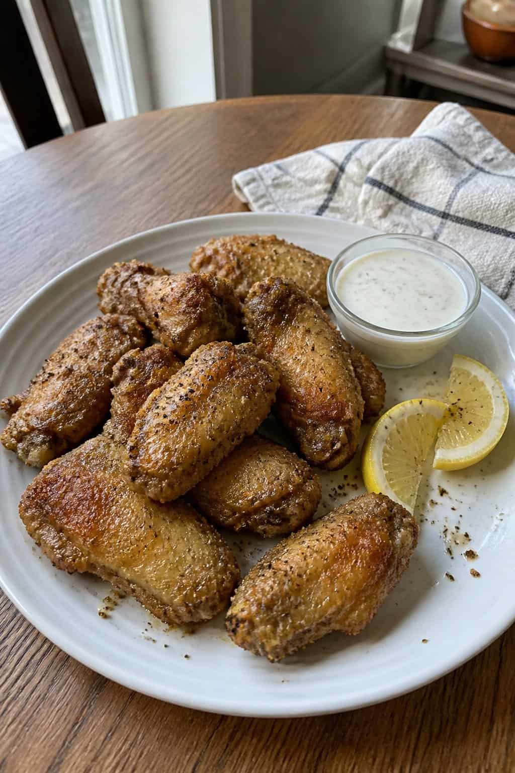 20 Copycat Chicken Recipes for Restaurant Cravings at Home 19 A plate of crispy lemon pepper chicken wings with lemon wedges and dipping sauce on a kitchen table.