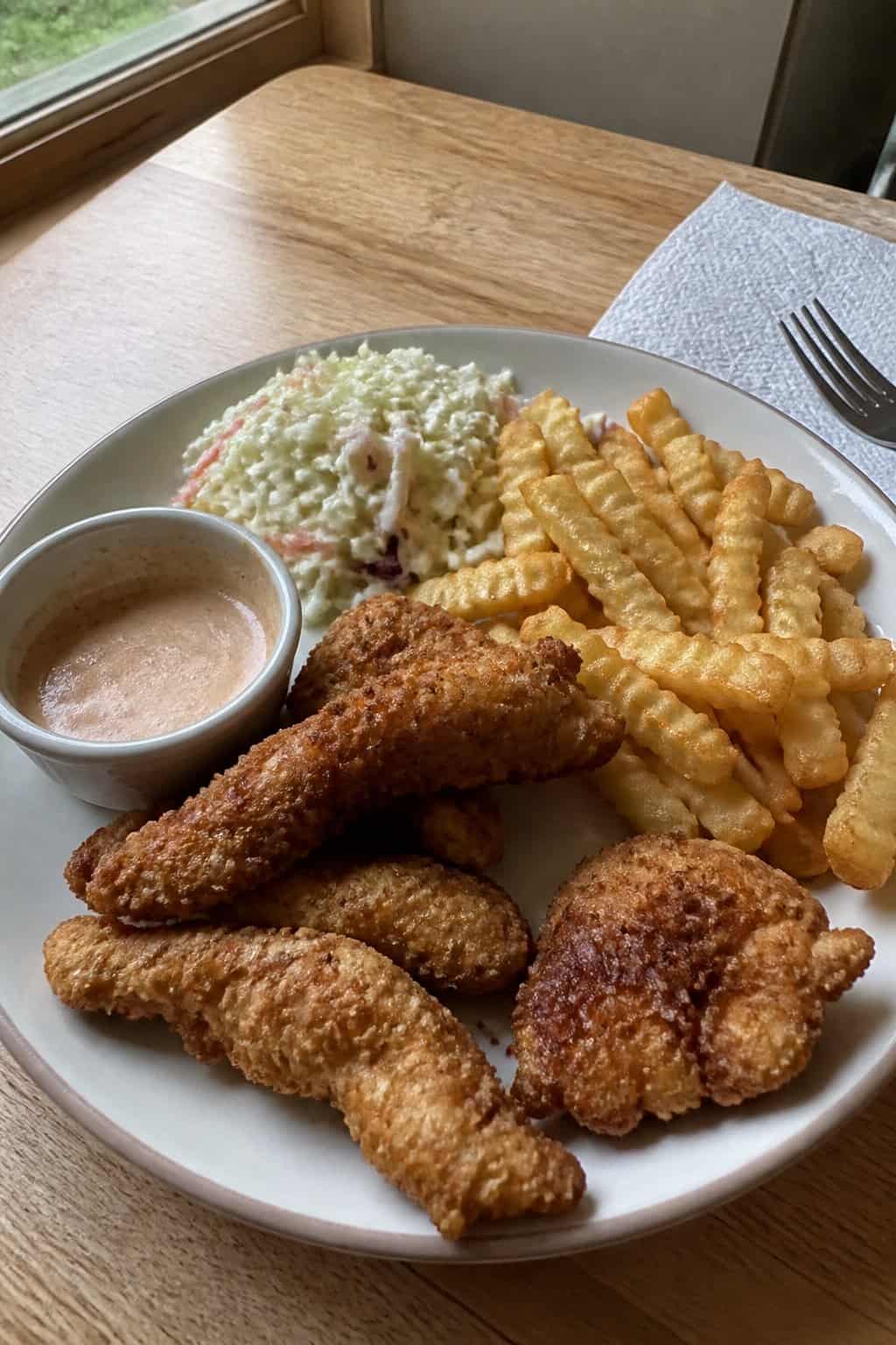 20 Copycat Chicken Recipes for Restaurant Cravings at Home 18 A plate of homemade chicken fingers with fries, coleslaw, and dipping sauce on a kitchen table.
