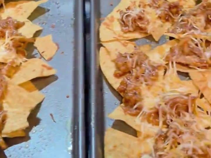 A baking tray of nachos with melted, bubbling cheese covering pulled pork and tortilla chips.
