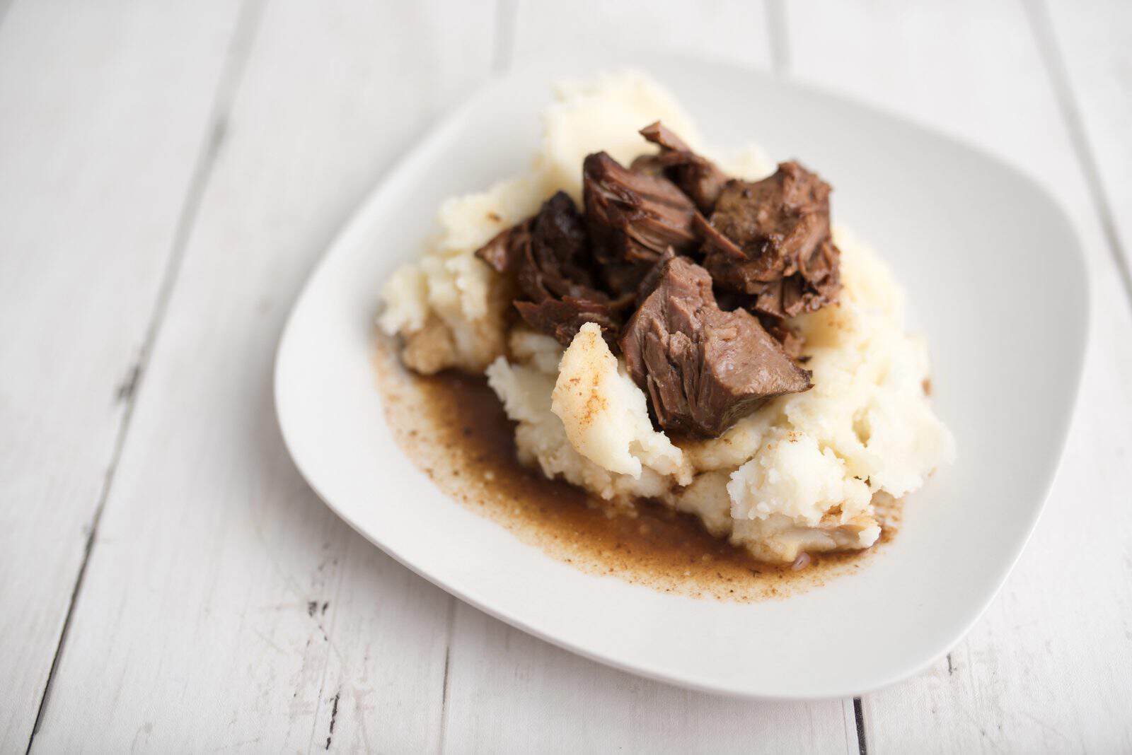 Crockpot Beef Recipes for Busy Weeknights 28 Beef pieces with brown gravy served over mashed potatoes on a white plate.
