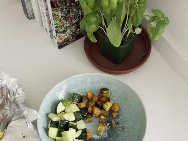 Two bowls each contain a portion of zucchini and roasted sweet potatoes, with space left in the bowl for salmon.