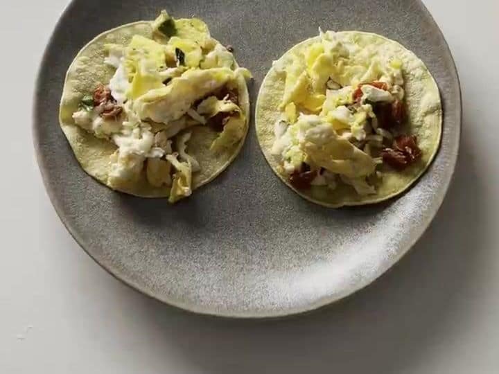 Italian Breakfast Tacos with Sun-Dried Tomatoes and Mozzarella 6 Scrambled eggs with melted cheese and sun-dried tomatoes spooned onto two tortillas on a gray plate.