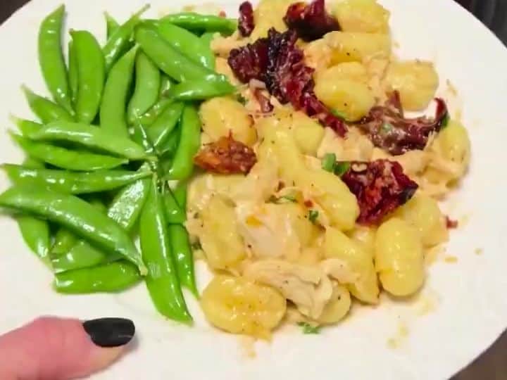 A plated serving of gnocchi with chicken, sun-dried tomato, and sugar snap peas on a white plate.