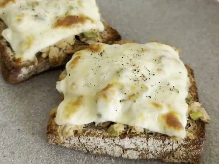 How to Make Tuna Melts with Pickles and Hot Sauce 7 Two finished tuna melt sandwiches with melted, golden cheese are plated together on a gray plate.