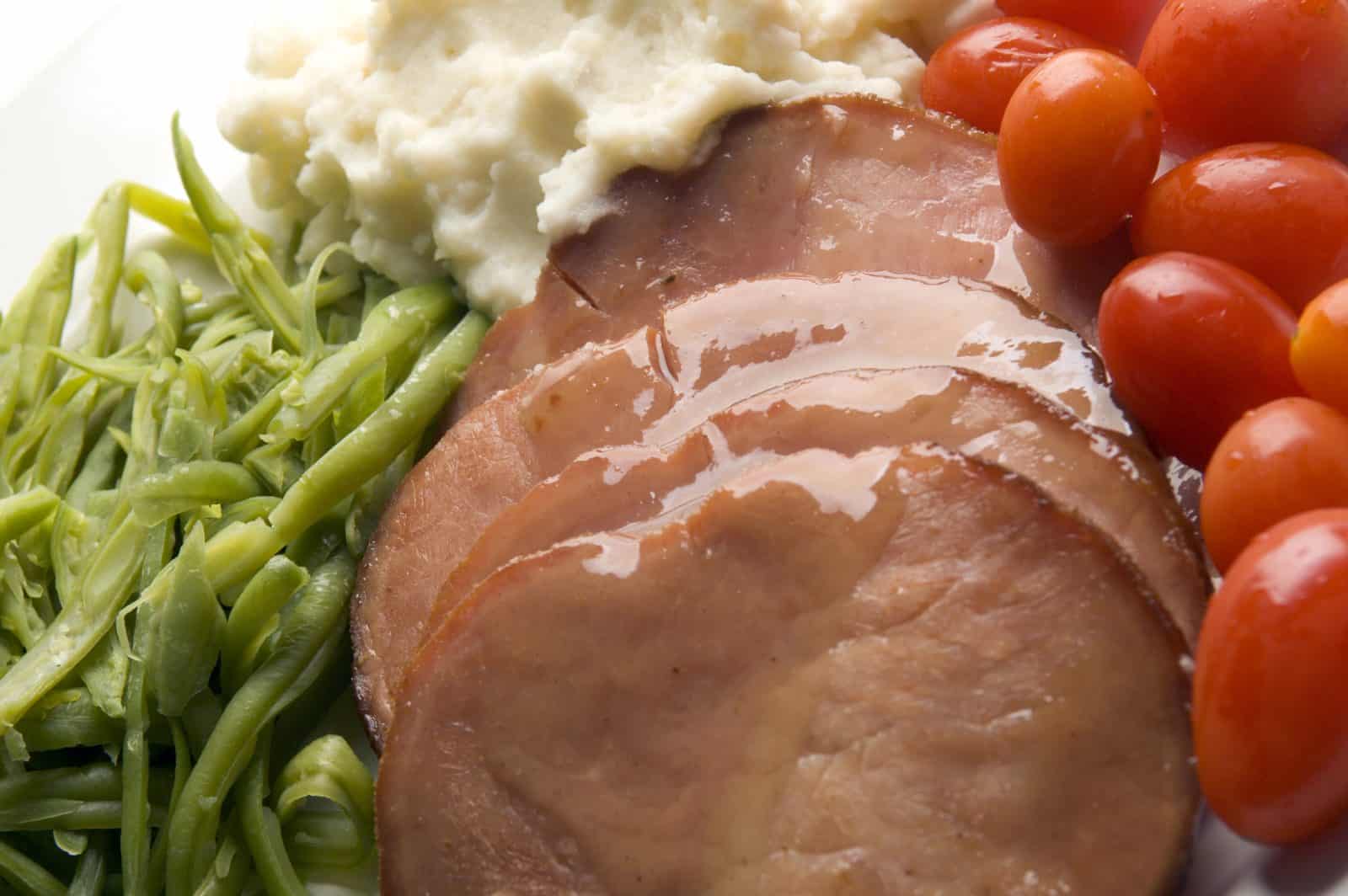 Sliced glazed ham with green beans and mashed potatoes
